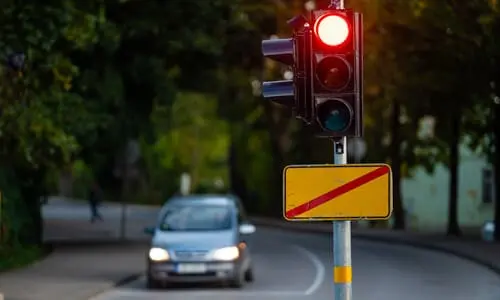 A selective focus shot of a car about to drive past a post with a traffic signal and light.