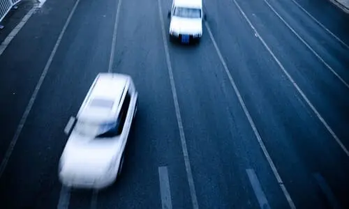 Two white vehicles performing dangerous lane changes in the early morning.