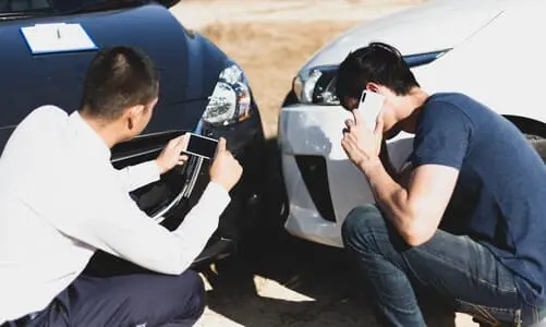A driver and his passenger each on their phones after a collision between two vehicles.