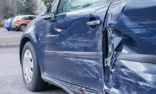 A blue family vehicle with a damaged left side door after a sideswipe accident.