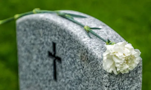 A wrongful death victim's tombstone with a white rose placed on top of it during a funeral.