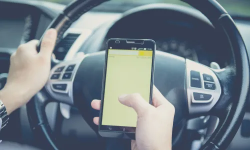 A first-person shot of a person driving a car while texting on their phone.