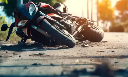 A motorcycle lying on its side after a crash on a suburban road with the sun glaring from behind.